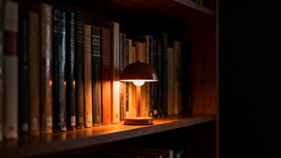 A small dome lamp glowing warm amber on a shelf of old books in a dark room