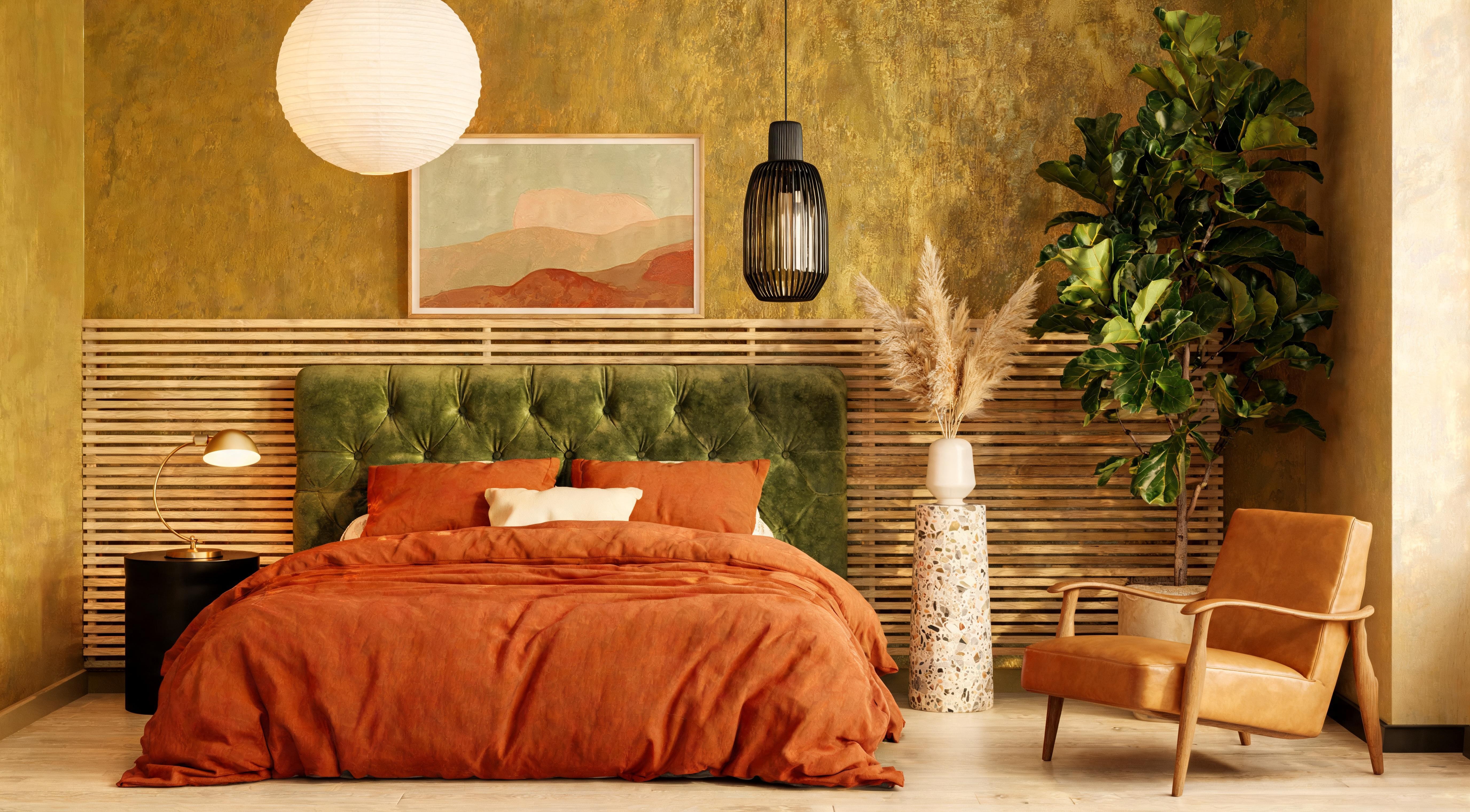 A warm ochre limewash bedroom with terracotta bedding, green velvet headboard and golden pendant lighting